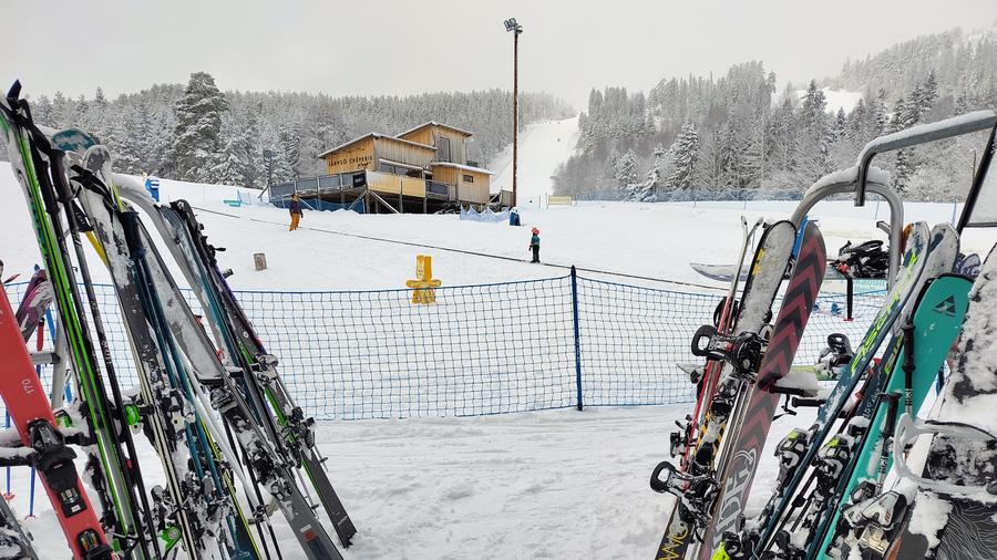 Skidor i ett skidställ i förgrunden och en skidbacke i bakgrunden
